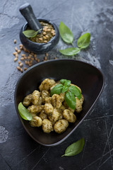 Potato gnocchi served with green basil pesto sauce in a black bowl over grey concrete background, vertical shot