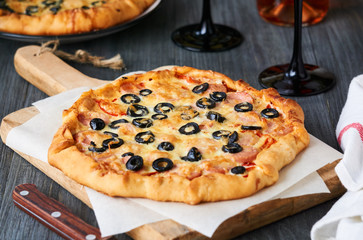 Homemade pizza with sausages, olives and cheese on a wooden board