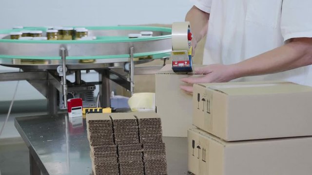 Worker packs glass jars with pesto sauce into cardboard box at food factory