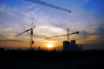 Silhouette of crane and building construction site in the city at sunrise.
