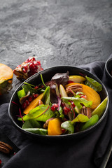 Persimmon salad with pear, pomegranate and pecan. Healthy vegetarian food concept.