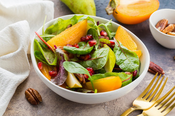 Persimmon salad with pear, pomegranate and pecan. Healthy vegetarian food concept.