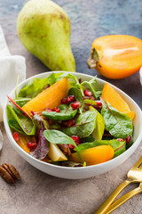Persimmon salad with pear, pomegranate and pecan. Healthy vegetarian food concept.