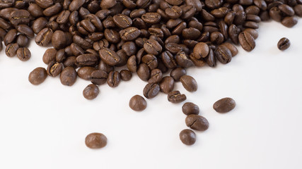 Brown, roasted coffee beans are shown up close and loosely spread out on a plain, white surface.