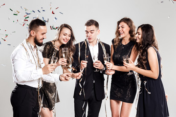 Company of  girls and guys dressed in stylish elegant clothes have fun together holding glasses of champagne and sparkles in hands on the white background confiture around. Party time