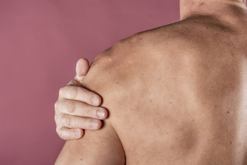 Naklejka premium Man holding his sore shoulder trying to relieve pain on pink background. Health problems