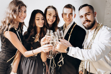 Beautiful young girls and guys dressed in stylish elegant clothes smile  together and clink glasses with champagne on a white background in the studio. Party time
