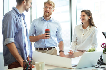 Obraz premium Young confident business people discussing something while looking at blueprint in the office, architecture team.