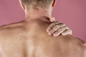 Naklejka premium Man holding his neck in pain, isolated on pink background. Lower neck pain. Shirtless man touching his neck for the pain