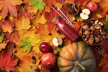 Autumn vegan and vegetarian food concept. Apples, pomegranate, nuts, spices, bottle of red drink - smoothie or juice over colorful leaves background. Picnic time. Top view