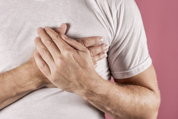 Fototapeta premium Man holding his chest with both hands, having heart attack or painful cramps, pressing on chest with painful expression on blue backgound. Severe heartache