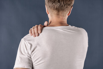 Man holding his sore shoulder trying to relieve pain on blue background. Health problems