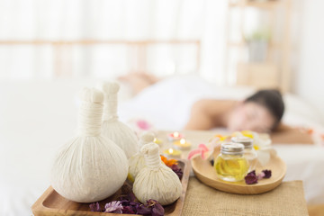 Selective focus of  Herbal compress balls with oil  on the wooden table in spa salon and blurred background of woman lying on bed.  alternative medicine and relaxation Concept.