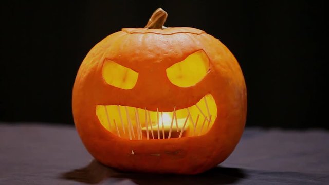Scary faced Jack-O-Lantern with flickering candle lighting the inside.  The pumpkin has toothpicks as teeth.  Evil grin with grill.