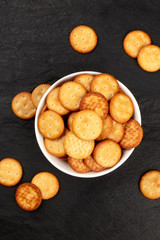 A photo of crispy salt crackers in a bowl, shot from above on a black background with copy space