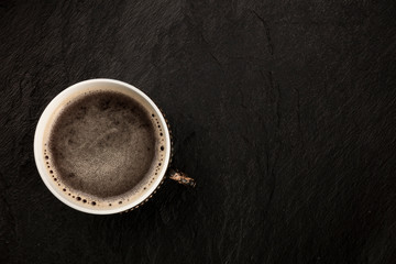 A photo of black coffee in a vintage cup, shot from above on a black slate background with copy space