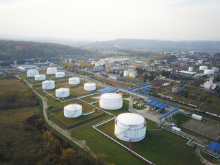 Naklejka premium Huge tanks with fuel and flammable substances on the territory of the refinery. View from the drone at a height of bird flight. The production of gasoline removed from aircraft. Oil refining industry.