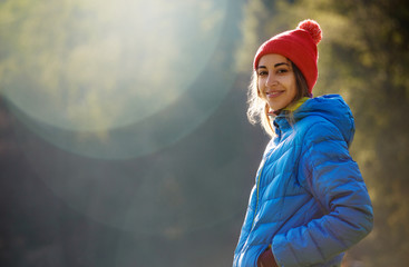happy smiling woman in a blue down jacket and red cap is standing in the autumn forest on a bright...