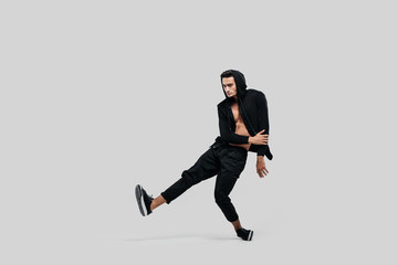 Young handsome young dancer dressed in black pants, a sweatshirt on a naked torso lifts one leg up while dancing street dance