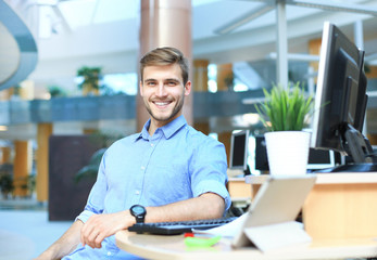 Portrait of happy man sitting at office desk, looking at camera, smiling.