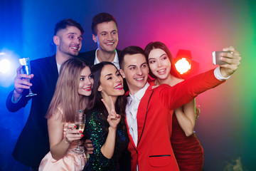 Group of happy friends celebrating new year with champagne and making selfie photo together on smart phone
