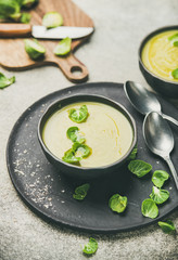 Seasonal brussels sprouts vegetable cream soup in dark bowl and fresh green brussel sprouts over grey concrete background, vertical composition. Vegan, vegetarian, healthy, dieting food concept