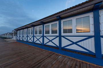 The exterior of wooden white and blue restaurant and wooden pathway on the beach. The dawn reflected on the windows.