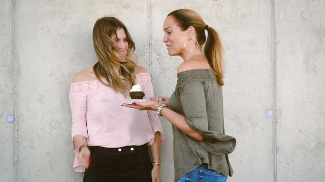 two very beautiful girlfriends celebrating birthday with muffin and having a lot of fun outdoor