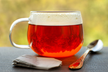 Hot tea with drops of steam on the windowsill. A glass cup of tea, tea bag, dessert spoon on the...
