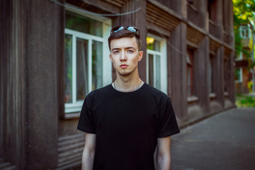 Portrait of sad and pensive handsome young man, wearing casual clothing standing near old brown building 