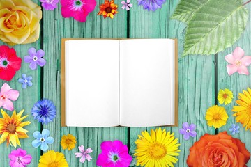 Beautiful flower frame with notepad in center on light blue desks of wood background. Floral composition of spring or summer flowers.
