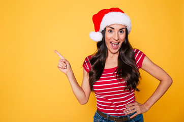 Fototapeta na wymiar Excited and emotional beautiful young cheerful woman in santa hat posing on yellow background