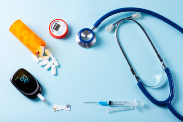 White pills in orange bottle with blood glucose meter ans stethoscope on blue background with copy...