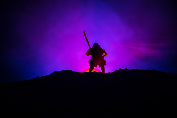 Fighter with a sword silhouette a sky ninja. Samurai on top of mountain with dark toned foggy background.