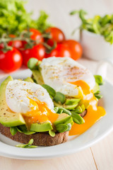 Avocado toast, cherry tomato and poached eggs on wooden background. Breakfast with vegetarian food, healthy diet concept.