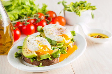 Avocado toast, cherry tomato and poached eggs on wooden background. Breakfast with vegetarian food, healthy diet concept.