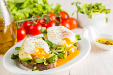 Avocado toast, cherry tomato and poached eggs on wooden background. Breakfast with vegetarian food, healthy diet concept.