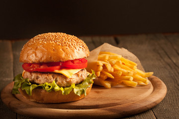 Home made hamburger with beef, onion, tomato, lettuce and cheese. Fresh burger close up on wooden rustic table with potato fries, beer and chips. Cheeseburger.