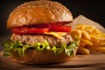 Home made hamburger with beef, onion, tomato, lettuce and cheese. Fresh burger close up on wooden rustic table with potato fries, beer and chips. Cheeseburger.