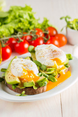 Avocado toast, cherry tomato and poached eggs on wooden background. Breakfast with vegetarian food, healthy diet concept.