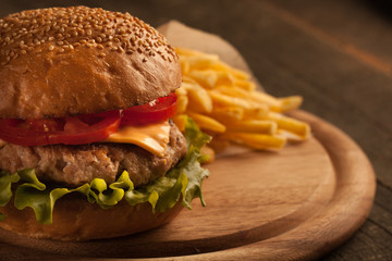 Home made hamburger with beef, onion, tomato, lettuce and cheese. Fresh burger close up on wooden rustic table with potato fries, beer and chips. Cheeseburger.