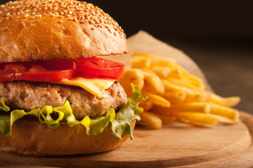 Home made hamburger with beef, onion, tomato, lettuce and cheese. Fresh burger close up on wooden rustic table with potato fries, beer and chips. Cheeseburger.