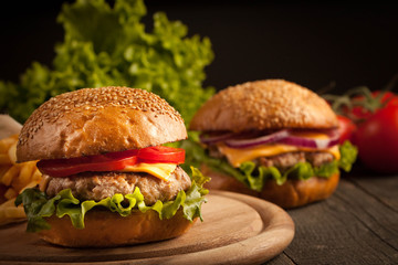 Home made hamburger with beef, onion, tomato, lettuce and cheese. Fresh burger close up on wooden rustic table with potato fries, beer and chips. Cheeseburger.