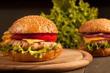 Home made hamburger with beef, onion, tomato, lettuce and cheese. Fresh burger close up on wooden rustic table with potato fries, beer and chips. Cheeseburger.