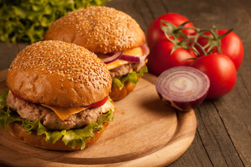 Home made hamburger with beef, onion, tomato, lettuce and cheese. Fresh burger close up on wooden rustic table with potato fries, beer and chips. Cheeseburger.