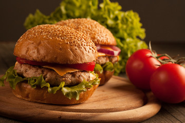 Home made hamburger with beef, onion, tomato, lettuce and cheese. Fresh burger close up on wooden rustic table with potato fries, beer and chips. Cheeseburger.