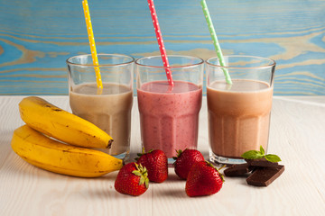 Long glasses of milkshakes with chocolate, strawberry, banana, with ice cream on white and blue...