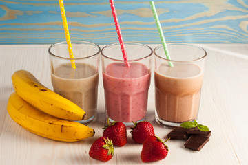 Long glasses of milkshakes with chocolate, strawberry, banana, with ice cream on white and blue...