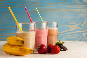 Long glasses of milkshakes with chocolate, strawberry, banana, with ice cream on white and blue...