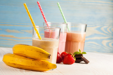 Long glasses of milkshakes with chocolate, strawberry, banana, with ice cream on white and blue background. Shakes and smoothies. Milk shake and cocktail for summer.